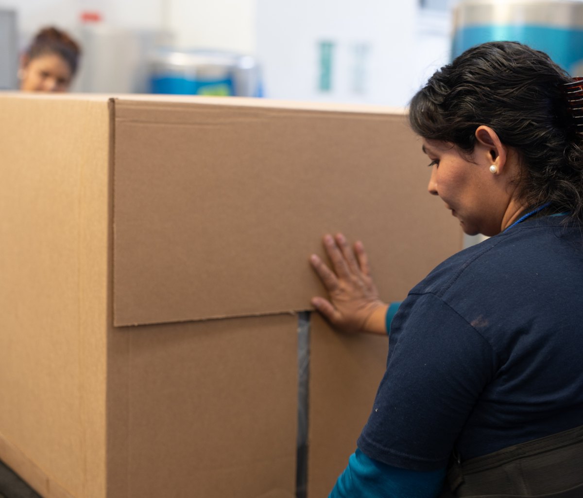 The image shows two Autopartes Tracto employees packing a product in an on-demand Packsize box